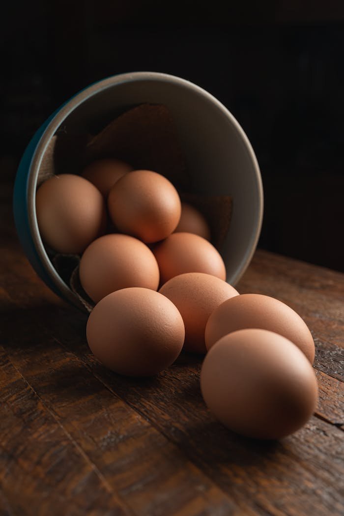 A dozen organic brown eggs spilling onto a rustic wooden surface, highlighting natural food simplicity.