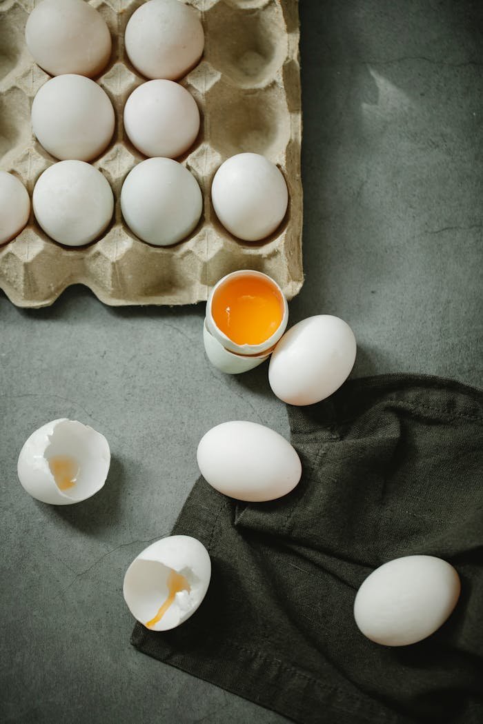 Top view composition of raw organic eggs placed in egg carton and scattered on dark table in kitchen